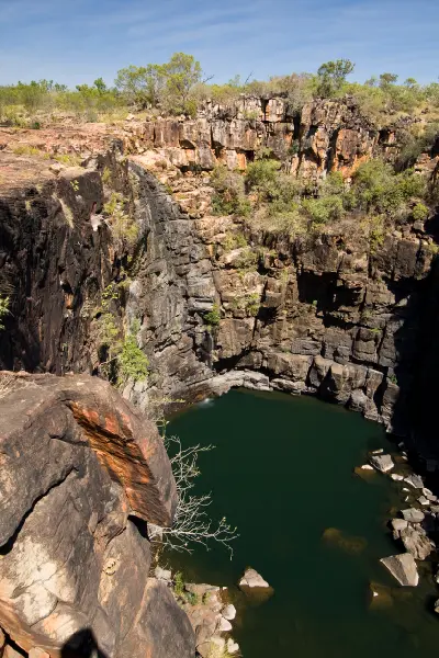 Deep plunge pool beneath the towering sandstone cliffs of Big Mertens Falls, with the waterfall reduced to a trickle during the dry season.