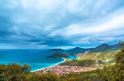 Elevated view from Babadağ over Ölüdeniz, Belcekız Beach and the Blue Lagoon beneath dramatic clouds in southwestern Türkiye.