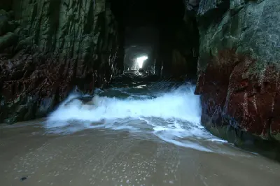 Ocean wave surging through the dark rock tunnel of Remarkable Cave, Tasmania.