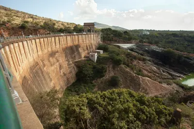 View of the curved Hartbeespoort Dam wall overlooking the Crocodile River gorge, with rocky cliffs, indigenous vegetation and the Magaliesberg mountains in the background.