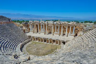 Well-preserved ancient Roman theatre at Hierapolis, with tiered stone seating surrounding an ornate columned stage and mountains in the distance.