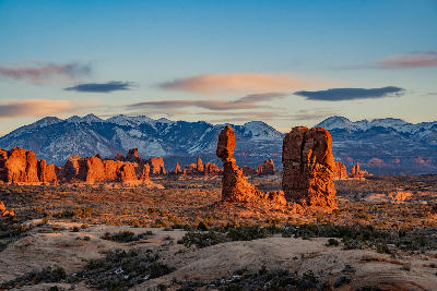 Balanced Rock illuminated by low sun with snow-capped La Sal Mountains and desert formations in Arches National Park Utah
