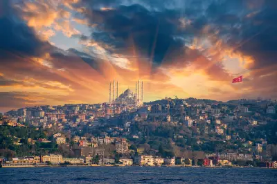View of Çamlıca Hill from across the Bosphorus, with Çamlıca Mosque and a large Turkish flag beneath a dramatic sunset sky.