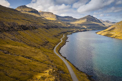 Empty coastal road running beside Funningsfjørður fjord with layered mountains on Eysturoy, Faroe Islands.