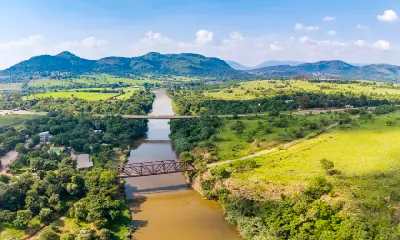 Aerial view of the Crocodile River flowing through Broederstroom with bridges, green farmland and the Magaliesberg mountains in the background.