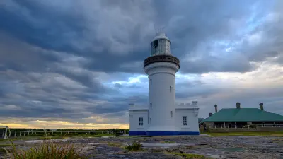 White Point Perpendicular Lighthouse and adjoining keeper’s buildings beneath dark storm clouds with warm light along the horizon.