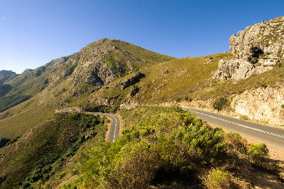 Curving roadway through Franschhoek Pass with steep mountain terrain and natural fynbos vegetation in the Cape Winelands of South Africa.