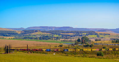 Freight train crossing farmland near the Nelson Mandela Capture Site outside Howick, with rolling hills and Midlands countryside in the background.