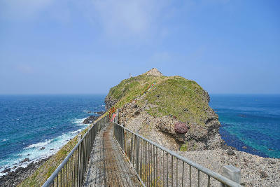 Narrow walkway with railings leading along a rocky ridge to the tip of Cape Kamui above the ocean in Shakotan, Hokkaido, Japan.