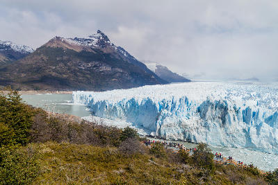Perito Moreno Glacier ice wall with visitors on boardwalk below and mountains in the background in Patagonia, Argentina.