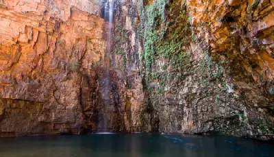 Waterfall drops from towering red rock walls into the dark plunge pool at the head of Emma Gorge.