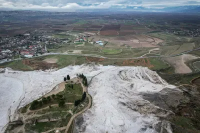 Aerial view over the white travertine formations of Pamukkale toward farmland, roads, villages, and distant mountains in Denizli Province, Turkey.