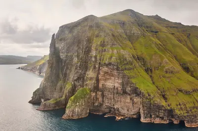 Trøllkonufingur sea stack, known as the Witch’s Finger, standing beside steep basalt cliffs on the coastline of Vágar Island near Sandavágur in the Faroe Islands.