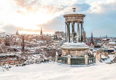 Dugald Stewart Monument on Calton Hill with the snowy skyline of Edinburgh and Edinburgh Castle in winter.