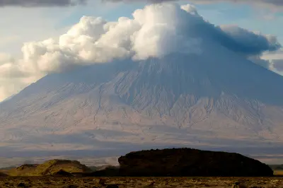 Ol Doinyo Lengai with its summit wrapped in thick clouds, towering above the arid plains near Lake Natron in the Great Rift Valley, Tanzania.