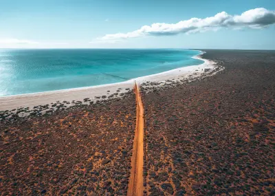 Aerial view of Shell Beach with a long white shoreline, turquoise water and a red dirt road crossing the surrounding scrubland.