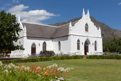 White Dutch Reformed Church in Franschhoek Village with Cape Dutch architecture, landscaped gardens, and mountains in the Western Cape.