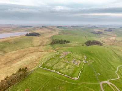 Drone view of the rectangular ruins and surviving stone foundations of Housesteads Roman Fort, surrounded by green hills and open Northumberland countryside.