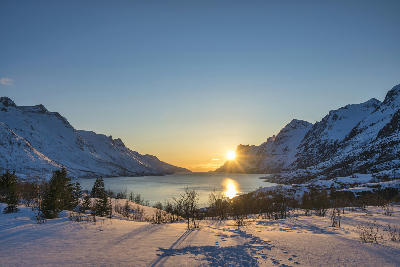 Ersfjord Senja Norway winter landscape with snow covered valley, fjord water and sunset light reflecting between mountain slopes.