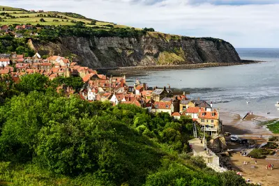 Elevated view of Robin Hood's Bay fishing village, with red-roofed cottages, a sandy beach, steep coastal cliffs and the North Sea in North Yorkshire, England.