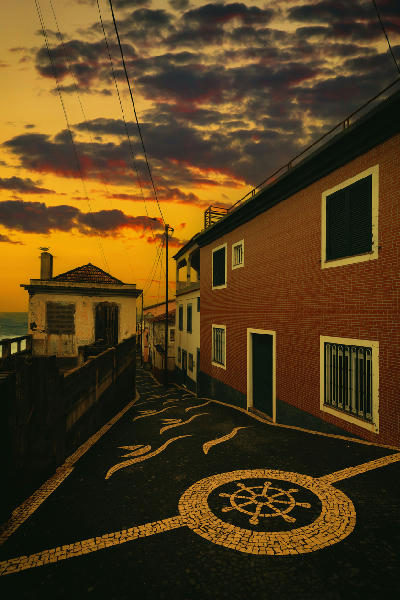 Cobblestone street in Paul do Mar at sunset, with traditional houses, patterned paving, and warm light reflecting off the Atlantic-facing buildings.