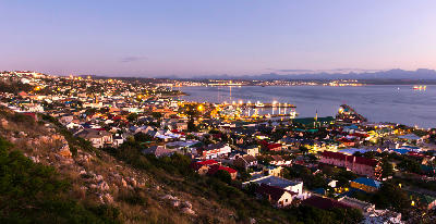 Evening view of Mossel Bay overlooking the harbour, town lights and coastline with the Outeniqua Mountains in the distance.