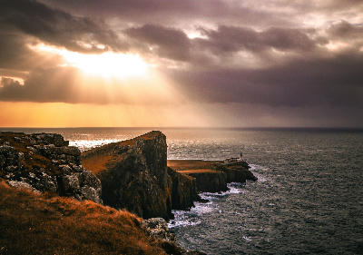 Neist Point Lighthouse on the Isle of Skye, bathed in golden light above rugged cliffs and the open sea in Scotland.