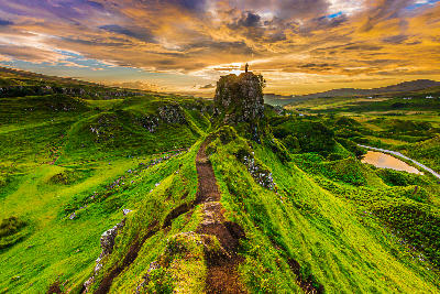 Sunset on the Isle of Skye in summer with Castle Ewen rock and a silhouette of a person at the top. Landscape in Scotland in the evening with clouds in the sky. path on the cliff edge