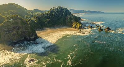 Aerial view of cliffs, green headlands, and ocean waves along the Oregon Coast.