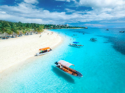 Aerial view of Kendwa Beach showing crystal-clear turquoise water, white sand, palm trees and anchored boats on Zanzibar's north coast, Tanzania.