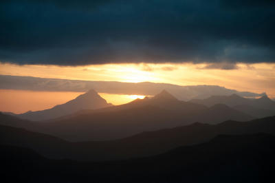 Sunset over Robinson Pass with dark storm clouds above layered mountain silhouettes in the Outeniqua Mountains.