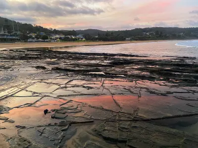 Tessellated coastal rocks and shallow tidal pools reflecting pink sunset light beside Lorne Beach, Victoria, Australia.