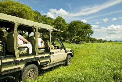 Open safari vehicle driving across the green floodplains of Katavi National Park, Tanzania.