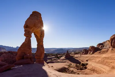 Delicate Arch backlit with sunburst and shadowed slickrock foreground in Arches National Park Utah