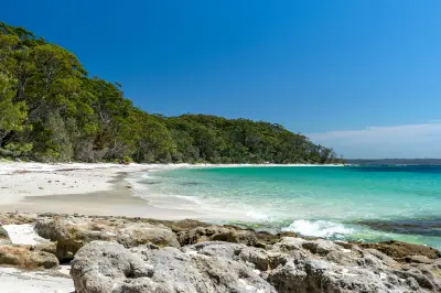 White sand, rocky shoreline and clear turquoise water at Murrays Beach, backed by dense coastal forest in Jervis Bay.