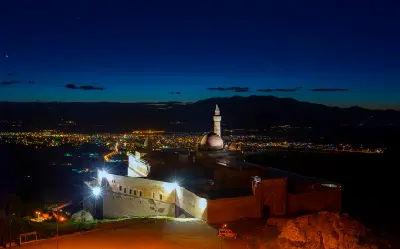 İshak Pasha Palace illuminated after dark with the lights of Doğubayazıt across the valley below.