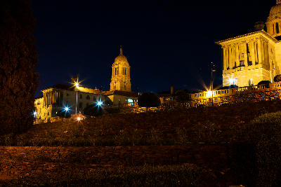 The Union Buildings glow under floodlights at night, with illuminated sandstone towers and terraced gardens overlooking Pretoria.