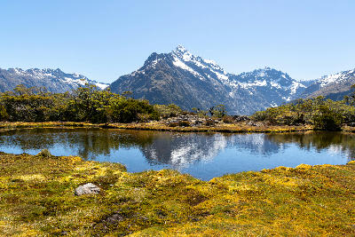 Alpine tarn on Key Summit with snow-capped mountains reflected in the water in Fiordland National Park, South Island, New Zealand.