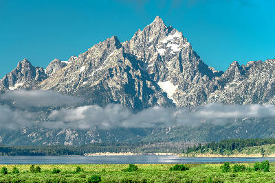Snow-capped Grand Teton peaks above Jackson Lake with a band of low cloud in morning light, Wyoming.