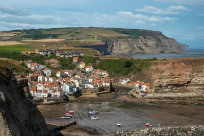 Elevated view of Staithes fishing village, its red-roofed cottages and boats at low tide, surrounded by cliffs on the North Yorkshire coast.