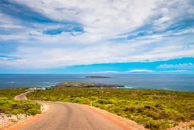 Winding Cape du Couedic Road leading towards Admirals Arch lookout through coastal heathland on Kangaroo Island, South Australia, with offshore islands in the distance.