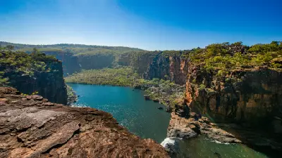 Final cascade of Mitchell Falls flowing into a deep turquoise pool enclosed by rugged sandstone cliffs and native vegetation.