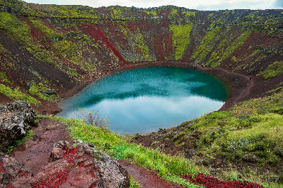 Kerið Crater lake on the Golden Circle in Iceland, showing steep red volcanic walls and a bright blue-green crater lake below.