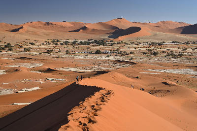 View from Big Daddy Dune across the red sand dunes of Sossusvlei in Namibia, with climbers walking along the dune ridge.