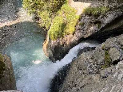Water surging through a narrow rock chute at Trümmelbach Falls, flowing into a turquoise river below in Lauterbrunnen Valley, Switzerland.