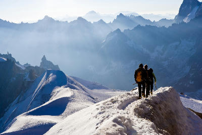 Climbers on a snow ridge in the Mont Blanc Massif near Chamonix, with layered alpine peaks fading into the distance.
