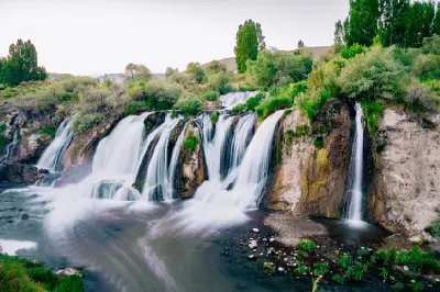 Wide view of Muradiye Waterfall cascading over rocky cliffs surrounded by lush green vegetation in Van Province, Turkey.
