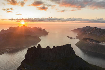 Midnight sun view from Grytetippen summit, Senja Norway, overlooking Mefjorden fjord and jagged peaks including Segla in warm evening light.
