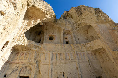 Ancient rock-cut Cave Church at the Göreme Open Air Museum in Cappadocia, Turkey, featuring carved arches, vaulted chambers, and Byzantine stone details beneath towering volcanic cliffs.