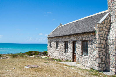 Traditional stone cottage with a thatched roof overlooking the ocean in Arniston on South Africa’s Western Cape coast.